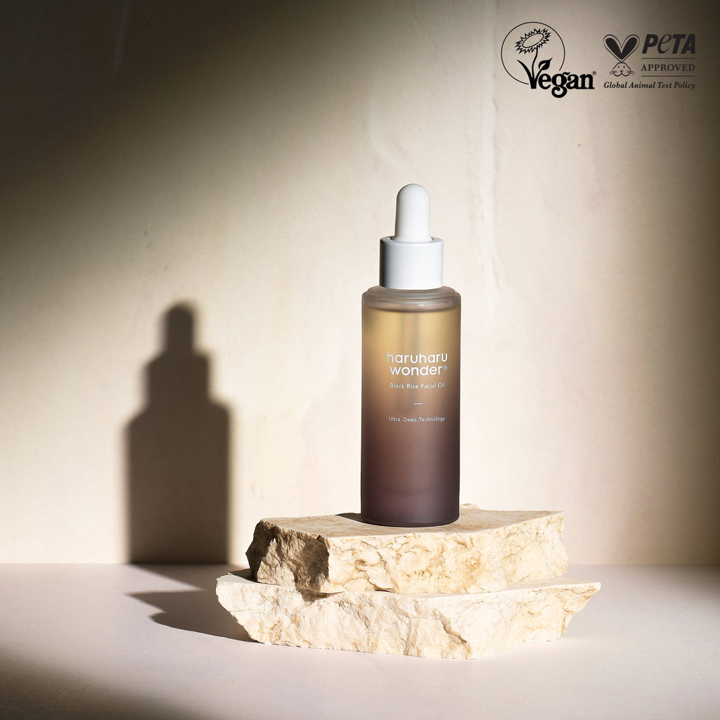 Haruharu Wonder Black Rice Facial Oil 30 ml bottle standing on layered stones in warm light.