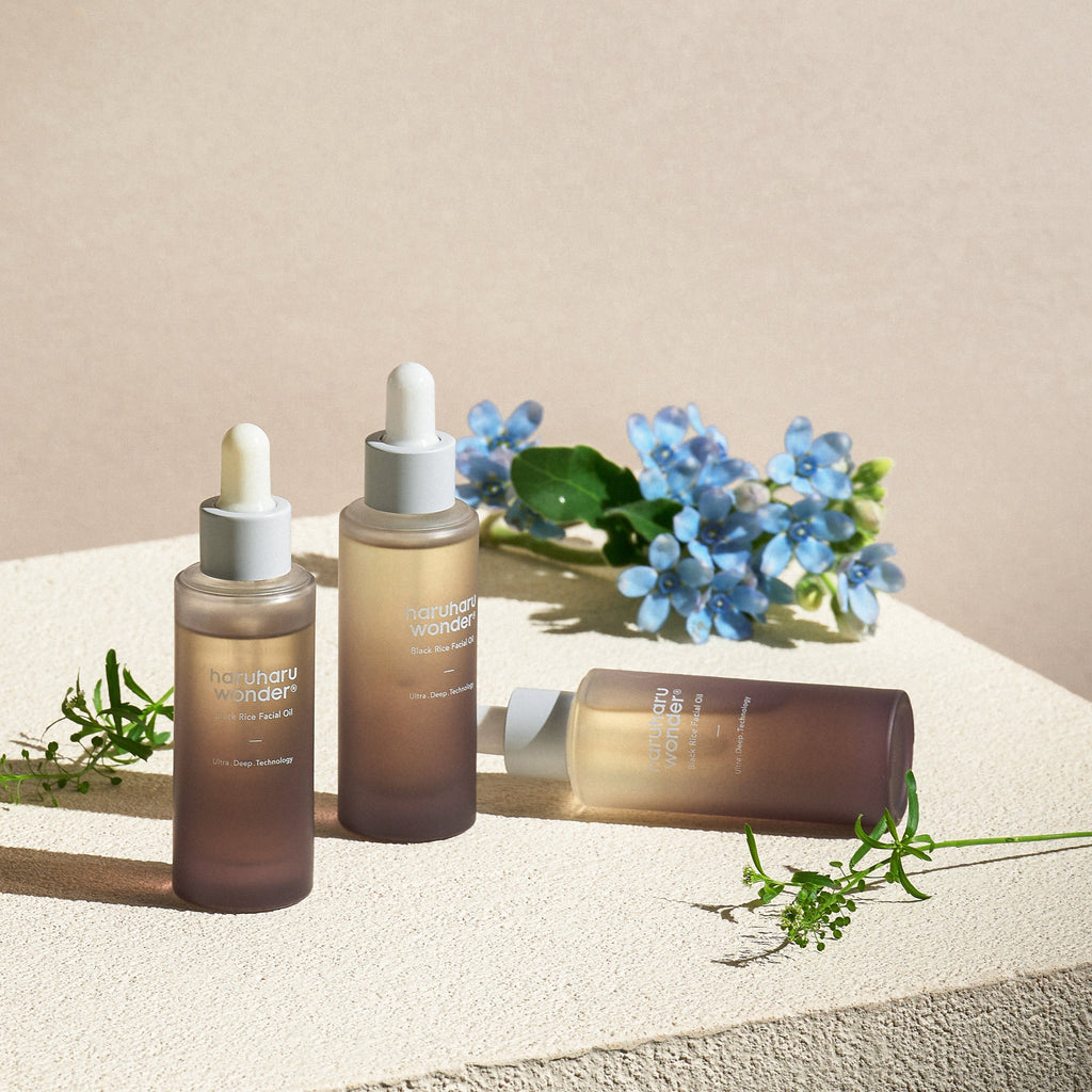 Haruharu Wonder Black Rice Facial Oil - 30ml — three 30 ml dropper bottles arranged on a sunlit surface with flowers.