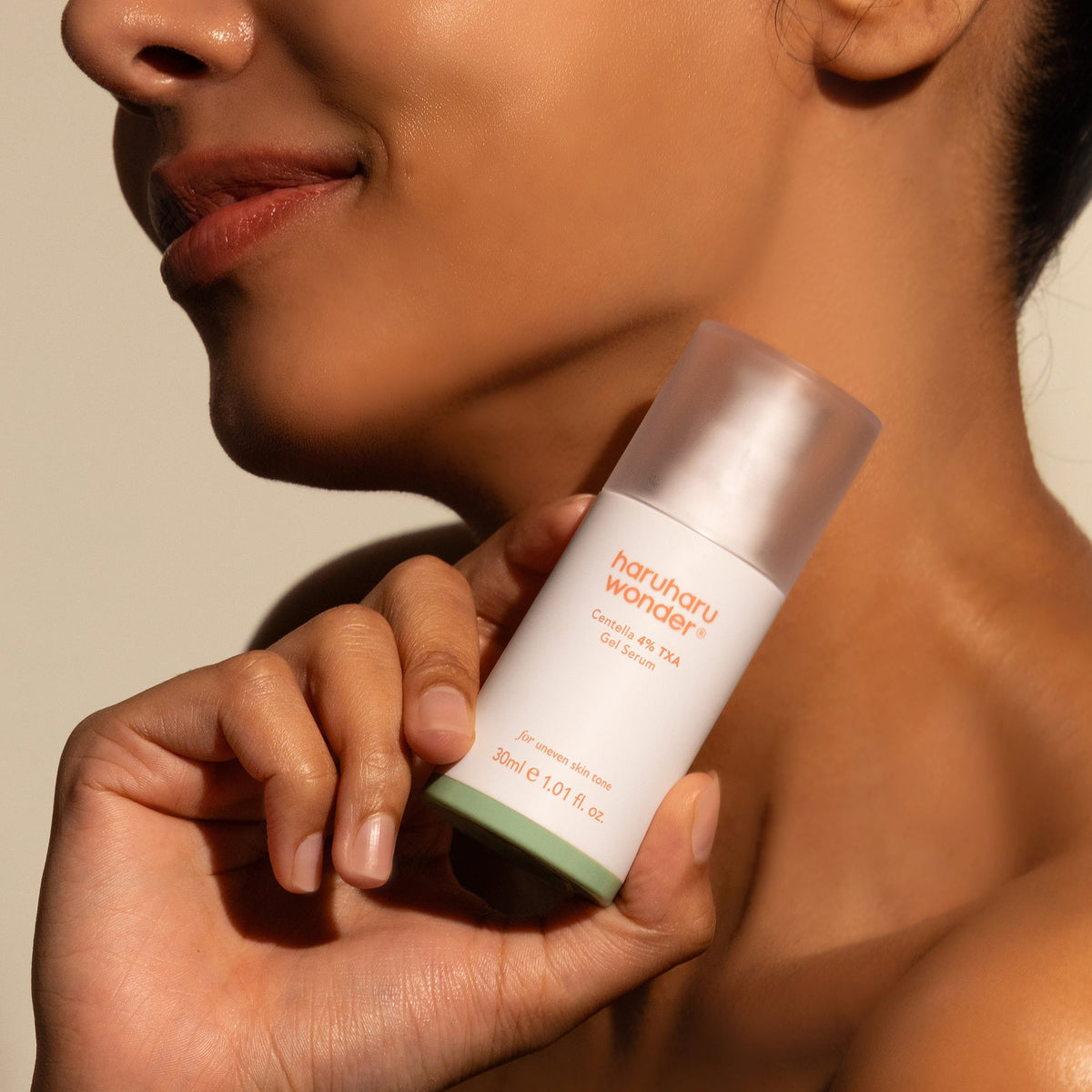 Haruharu Wonder Centella 4% TXA Gel Serum - 30ml — model holding the 30 ml TXA gel-serum bottle below her chin.