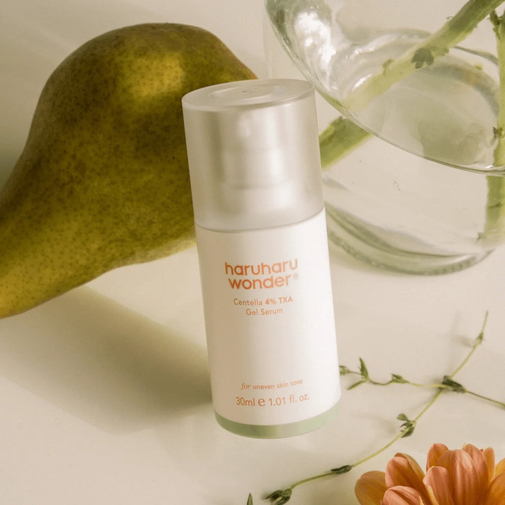 Haruharu Wonder Centella 4% TXA Gel Serum - 30ml — 30 ml TXA serum bottle beside a pear, clear glass and white flowers.