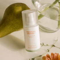 Haruharu Wonder Centella 4% TXA Gel Serum - 30ml — 30 ml TXA serum bottle beside a pear, clear glass and white flowers.