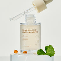 Heveblue Salmon Caring Centella Ampoule 30 ml, with the open bottle and liquid-filled dropper beside centella leaf props.