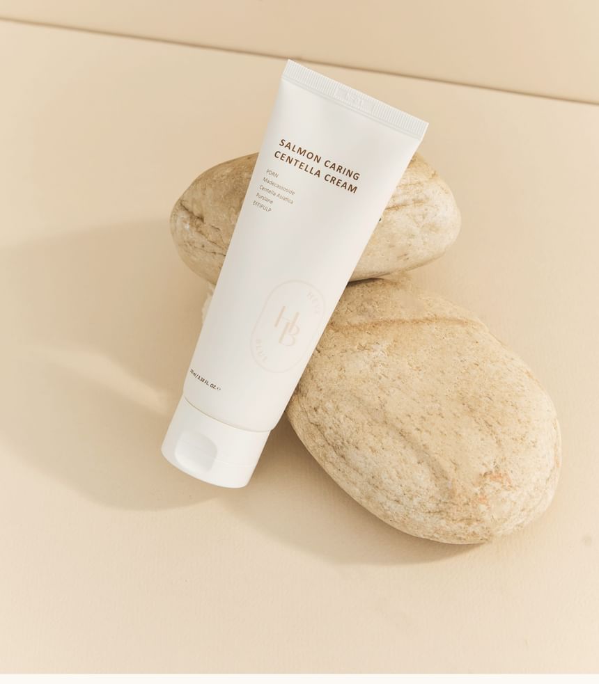 Heveblue Salmon Caring Centella Cream 100 ml — cream tube on a textured pedestal.