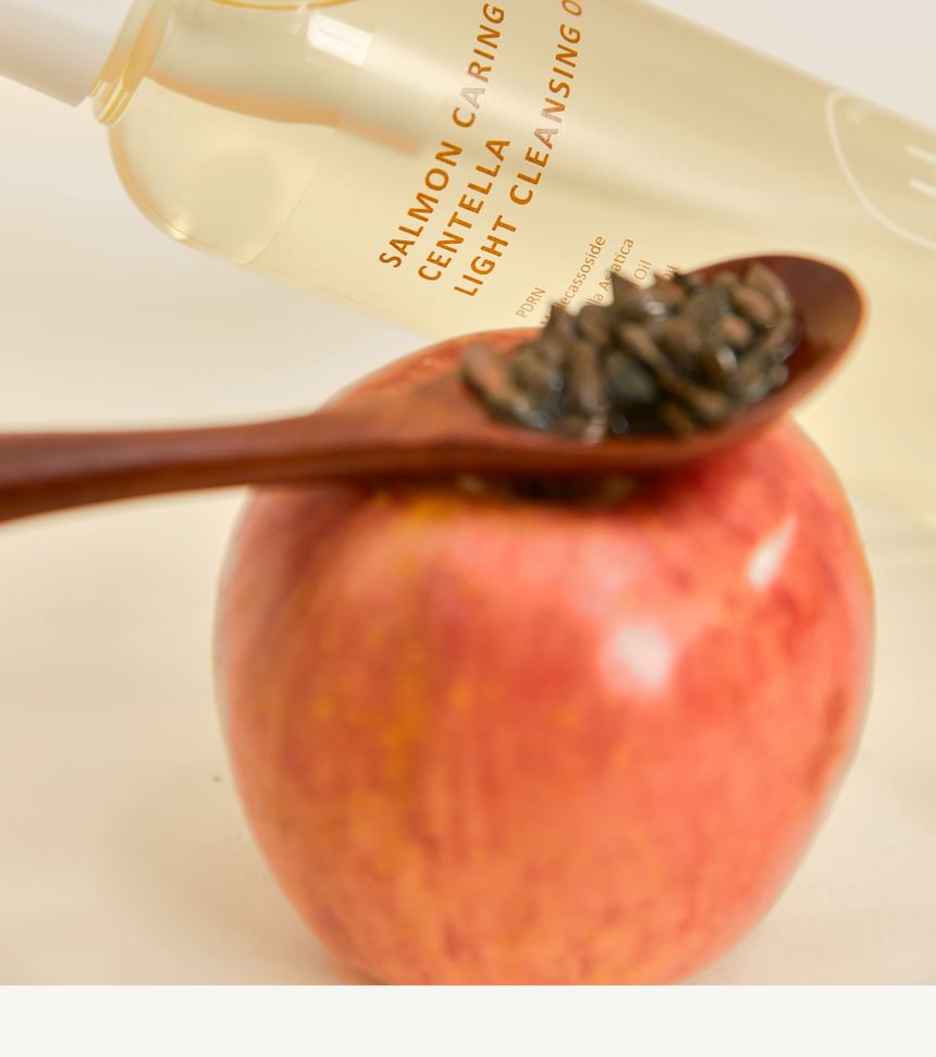Heveblue Salmon Caring Centella Light Cleansing Oil - 250ml — bottle beside apple seeds.
